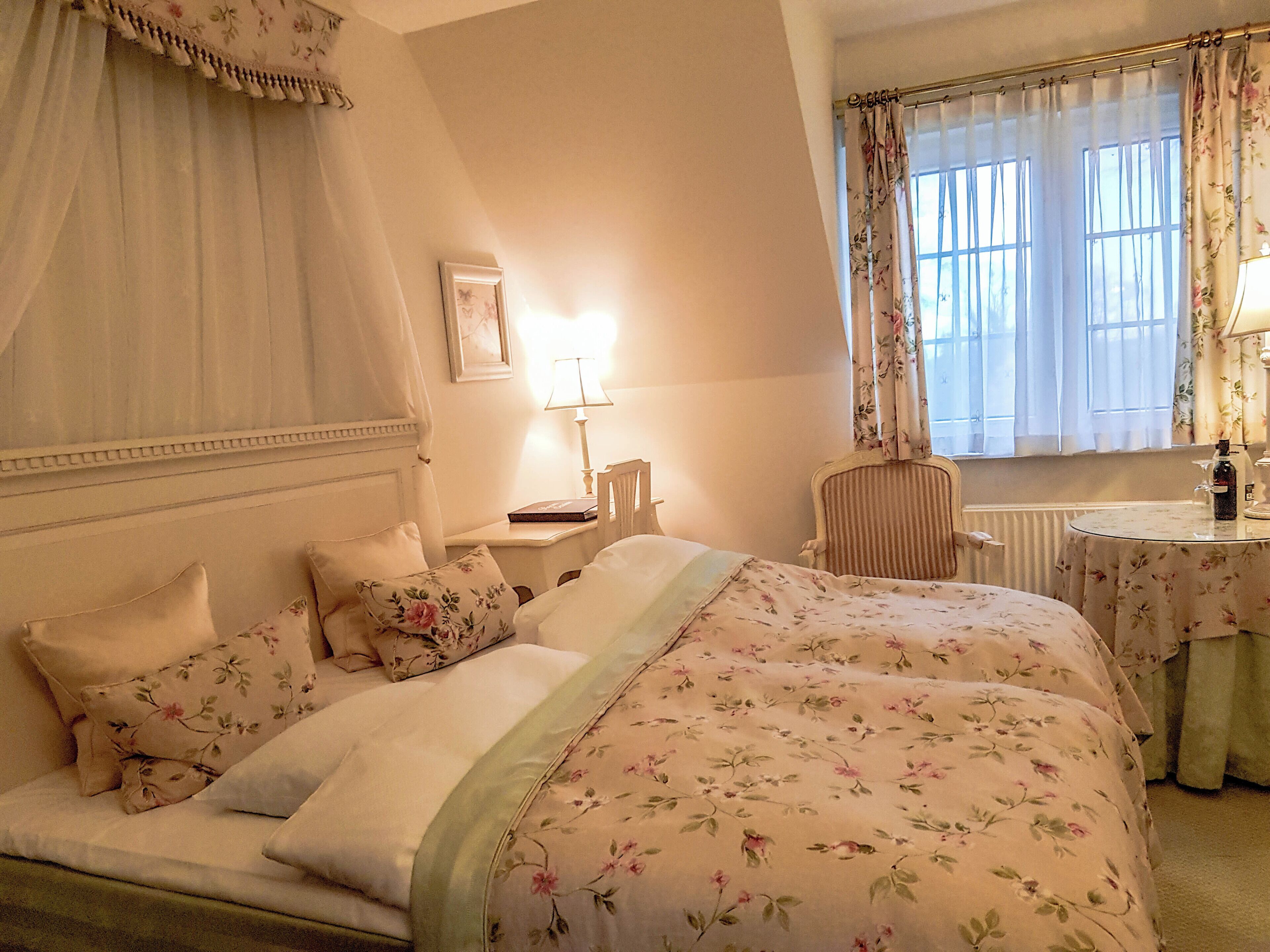 A bedroom with a bed, a chair, a table, and a window with curtains.