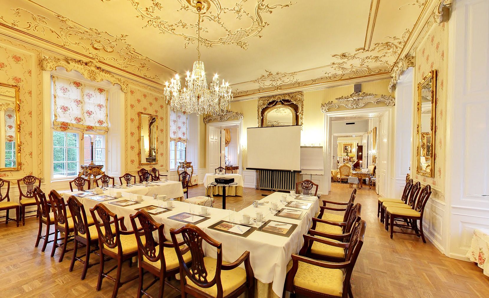 A formal dining room with ornate decor, a chandelier, and a long table set for a meal.