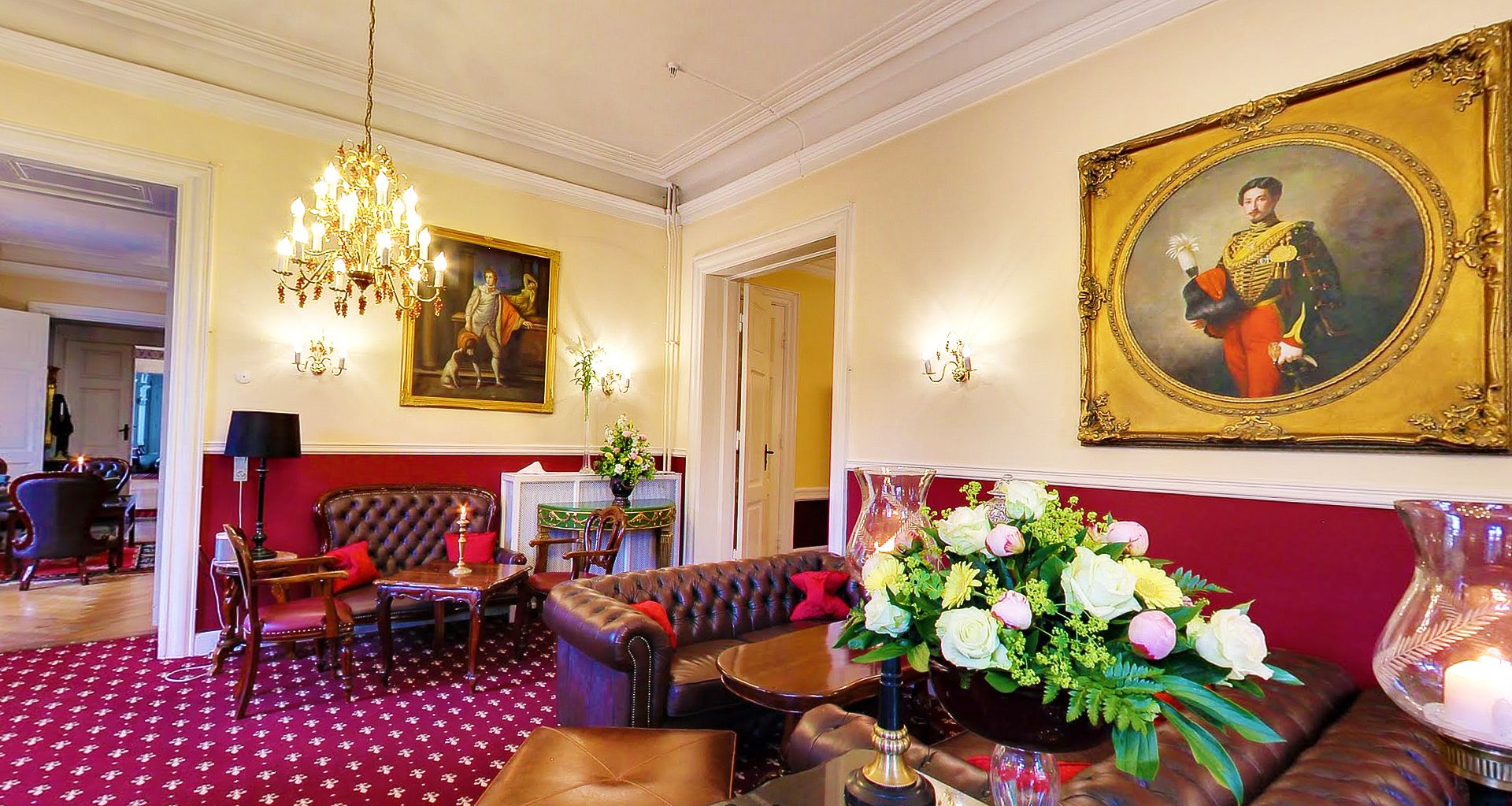 Un salon élégant, doté de canapés en cuir, d’un lustre et d’un grand portrait accroché au mur.