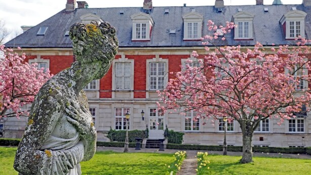 A stone statue in a garden with a large building in the background.