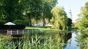 A serene park with a pond, a wooden bridge, and a distant building with a tower.