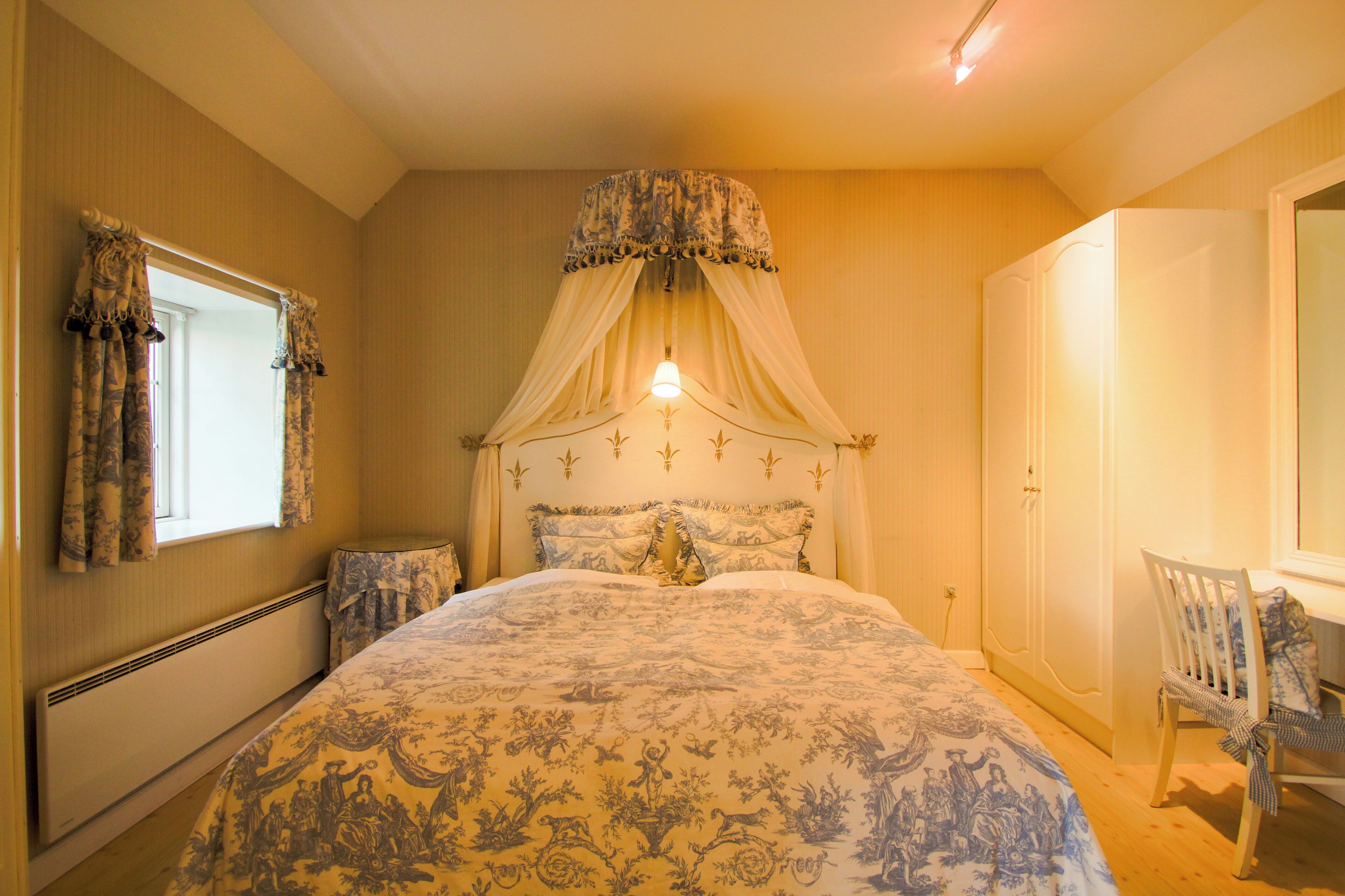 A bedroom with a large bed, a canopy bed, a chair, and a wardrobe.