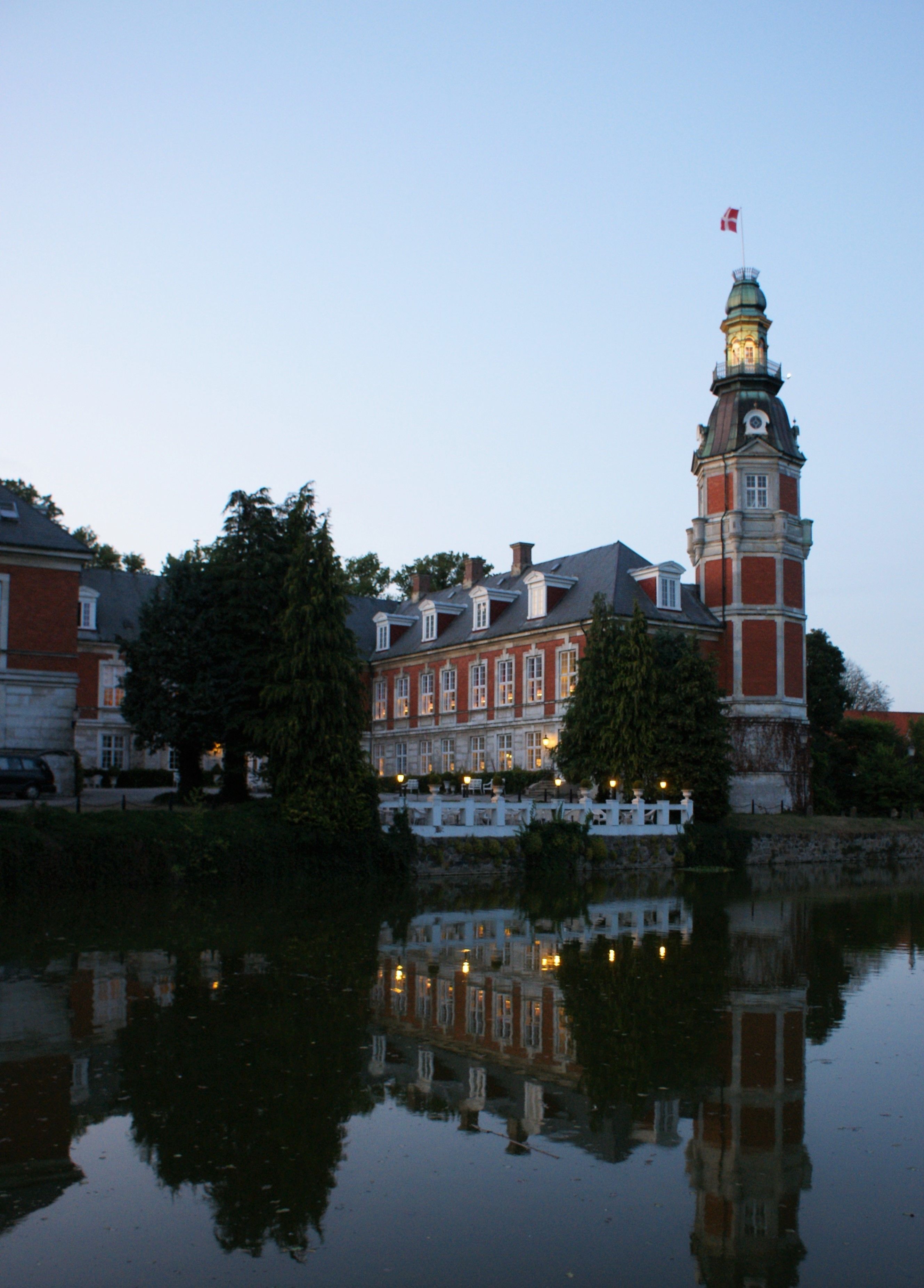 Un edificio histórico con una torre destacada, reflejado en aguas tranquilas.