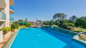 A swimming pool with a clear blue water, surrounded by a building with balconies and a view of the cityscape in the background. - Argyle on the Park (Maroochydore)