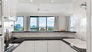 A modern kitchen with white cabinets, a black countertop, and a large window offering a city view. - Argyle on the Park (Maroochydore)