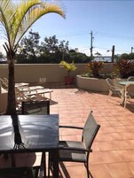 Un patio al aire libre con piso de baldosas, una mesa con sillas y plantas en macetas.