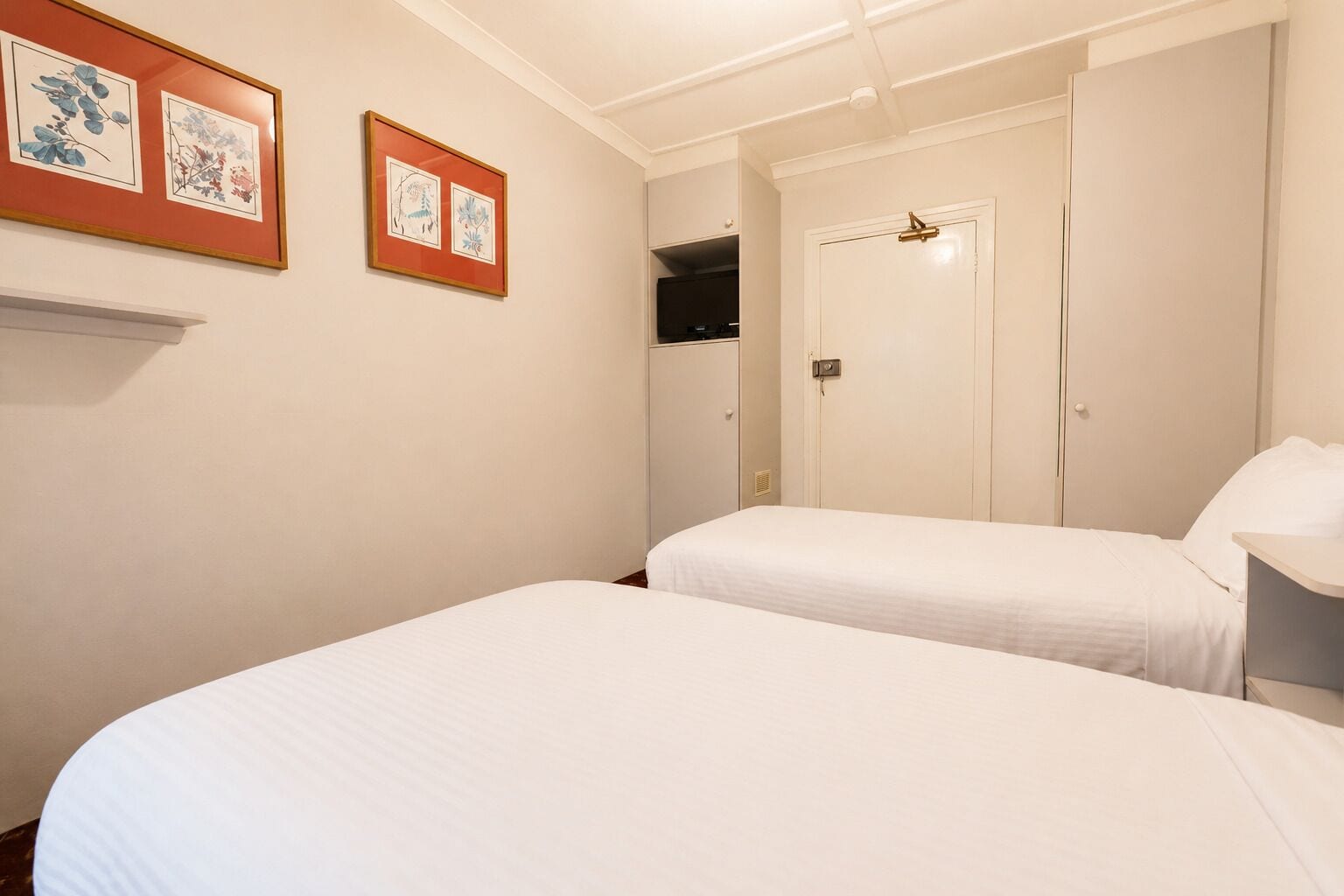Una habitación de hotel con dos camas, un armario y obras de arte botánicas enmarcadas en la pared.