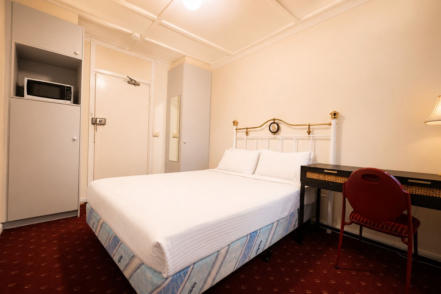 Una habitación de hotel con cama, escritorio, silla, armario y espejo.