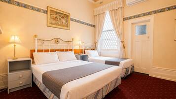 A hotel room with two beds, a nightstand, a lamp, a window with curtains, a door, and a wall-mounted picture.