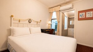 Habitación de hotel con una cama grande, un escritorio con silla, una ventana con cortinas y un baño visible a través de una puerta abierta.