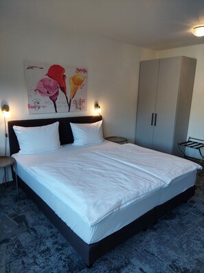 A neatly made bed with white linens, a headboard with two wall-mounted lights, a large grey wardrobe, and a wall-mounted artwork of flowers. - Hotel Stadt Gernsbach (Gernsbach)