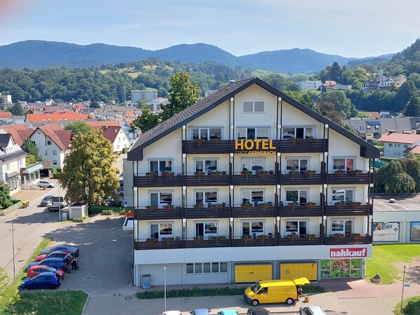 A hotel with a two-story structure, balconies with flower boxes, and a parking area with several cars. - Hotel Stadt Gernsbach (Gernsbach)
