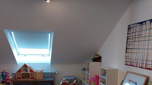 Een kinderspeelkamer met een hoogslapbed, letters van foam, een schommelpaard en een treinbaan met speelgoed.