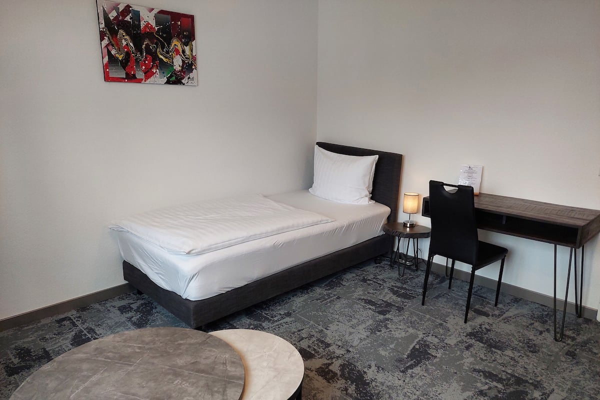 A hotel room with a bed, a desk, a chair, and a small table.