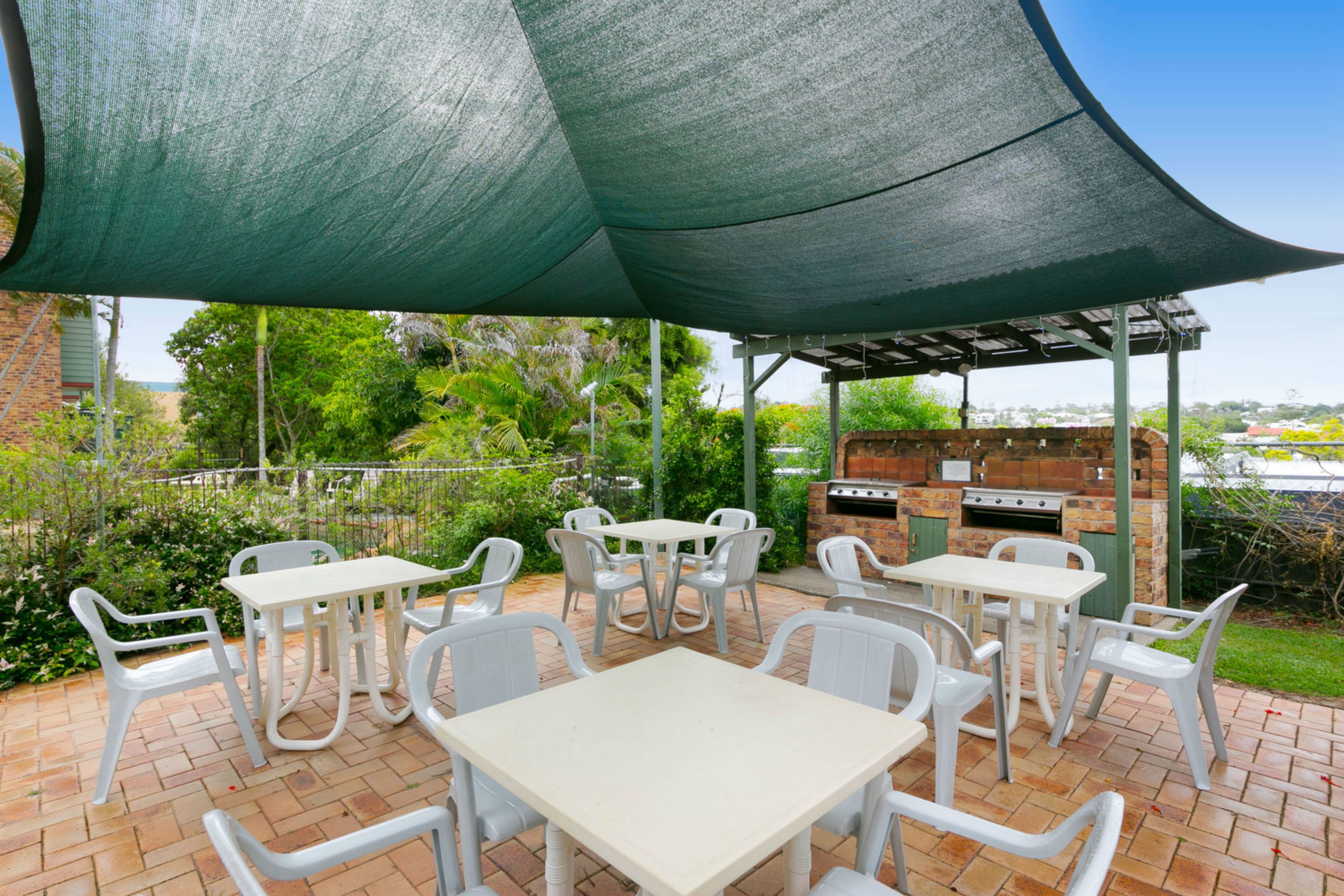 An outdoor patio with white plastic chairs and tables, a green canopy, and a brick barbecue area.