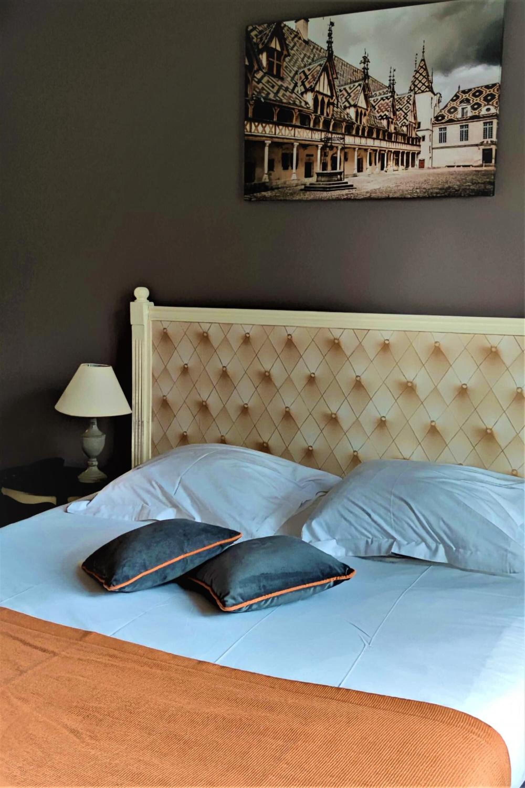 A hotel room with a bed, pillows, a lamp, and a painting on the wall.