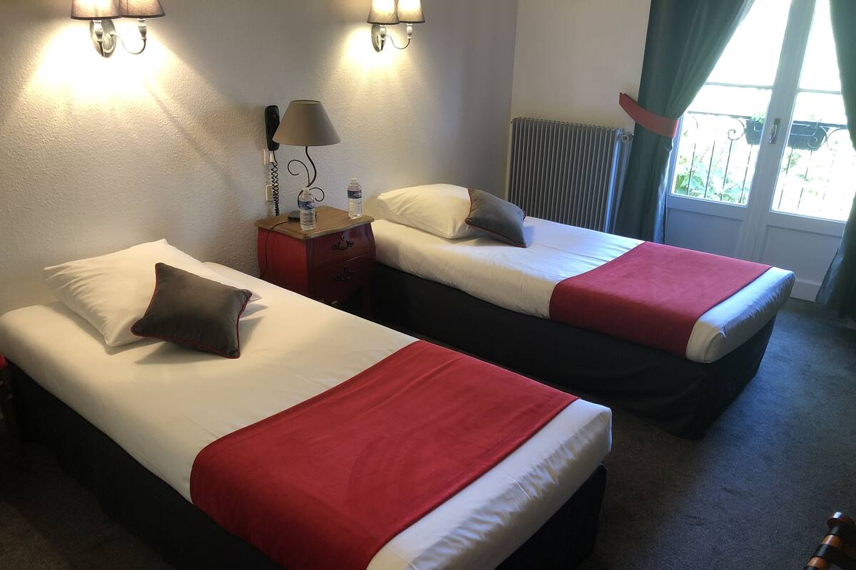 Two single beds with red and white bedding, a nightstand with a lamp, a water bottle, and a phone.