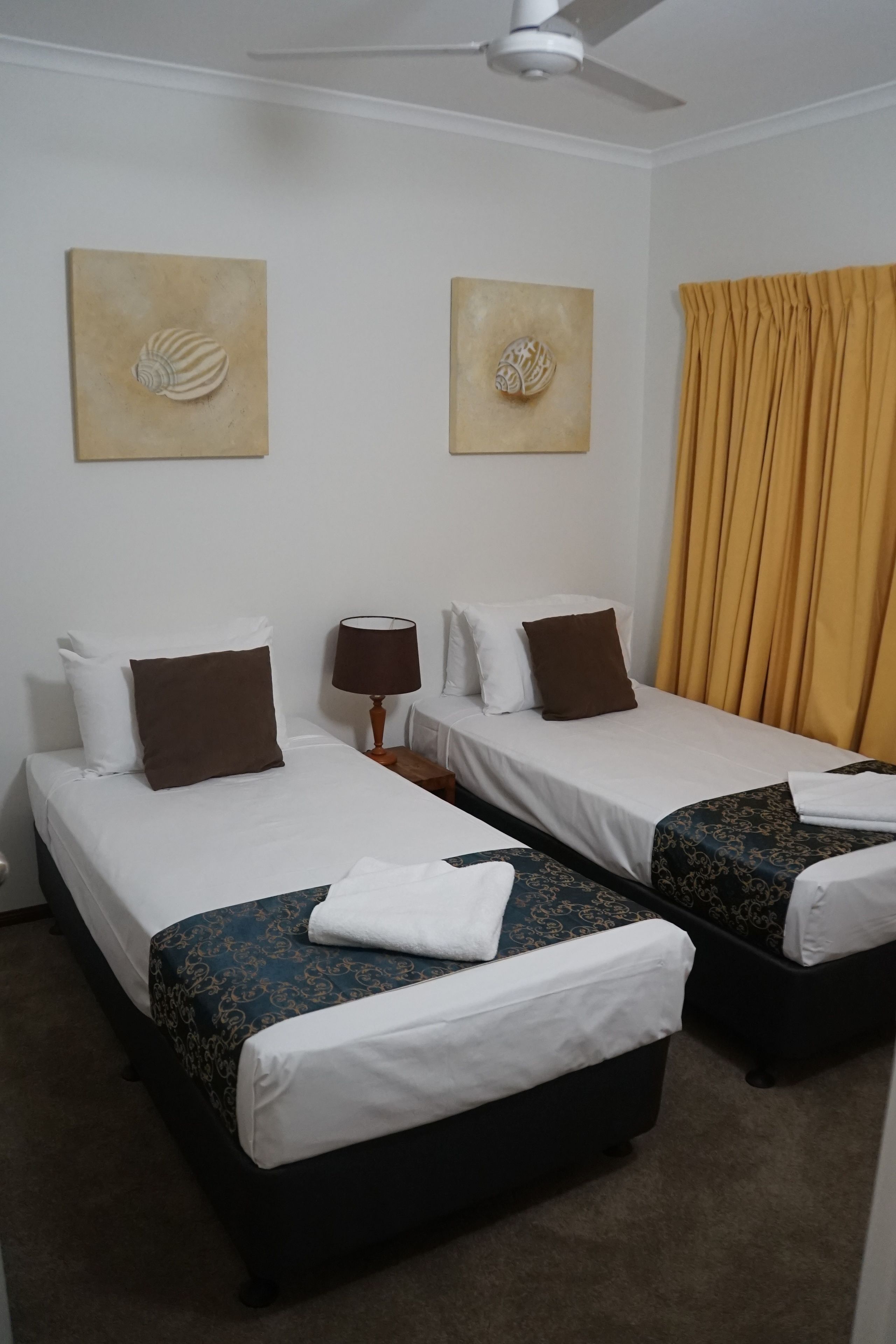 Ett hotellrum med två sängar, en takfläkt och konstverk på väggarna.