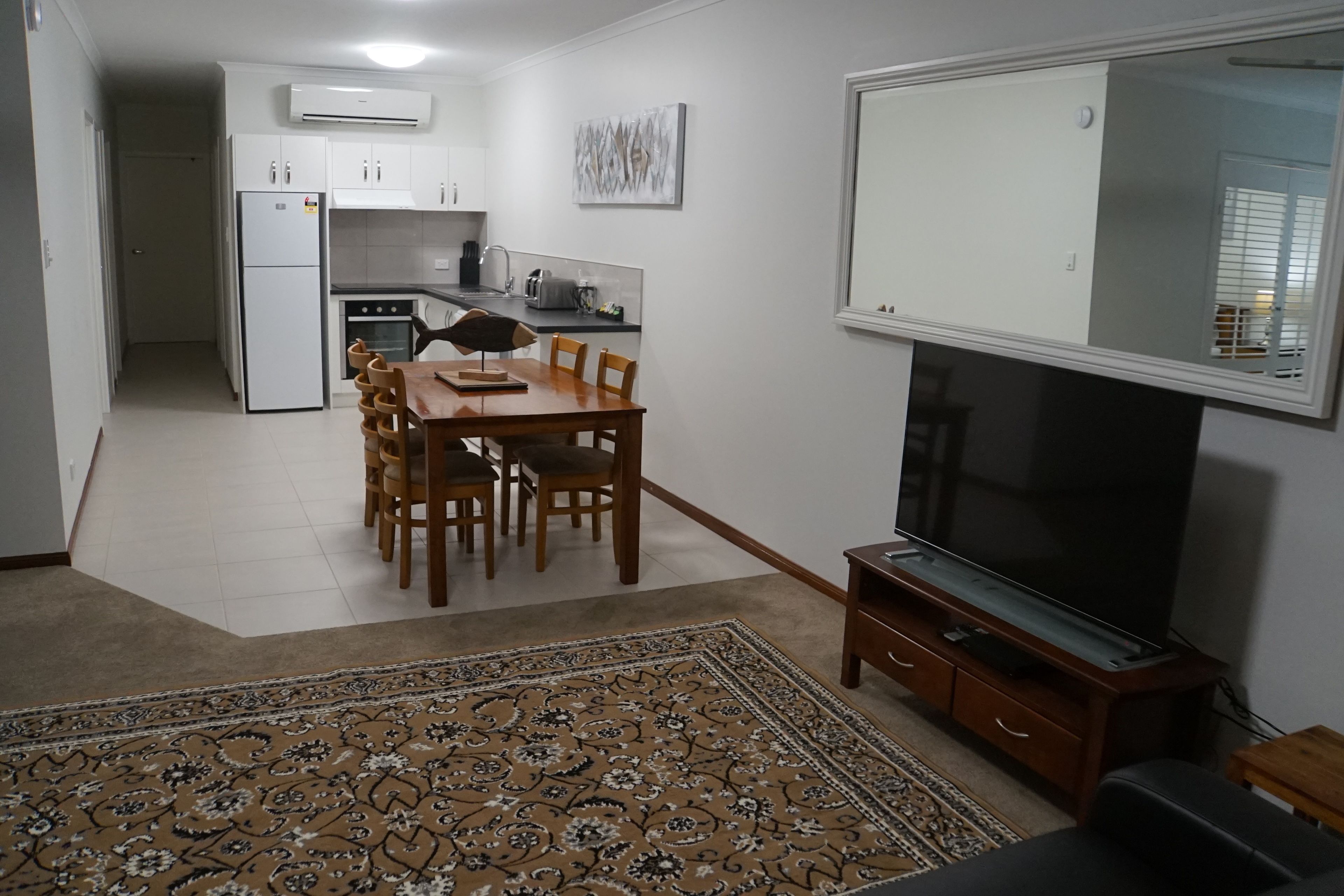 A compact living space with a dining area, kitchen, and a large flat-screen TV.