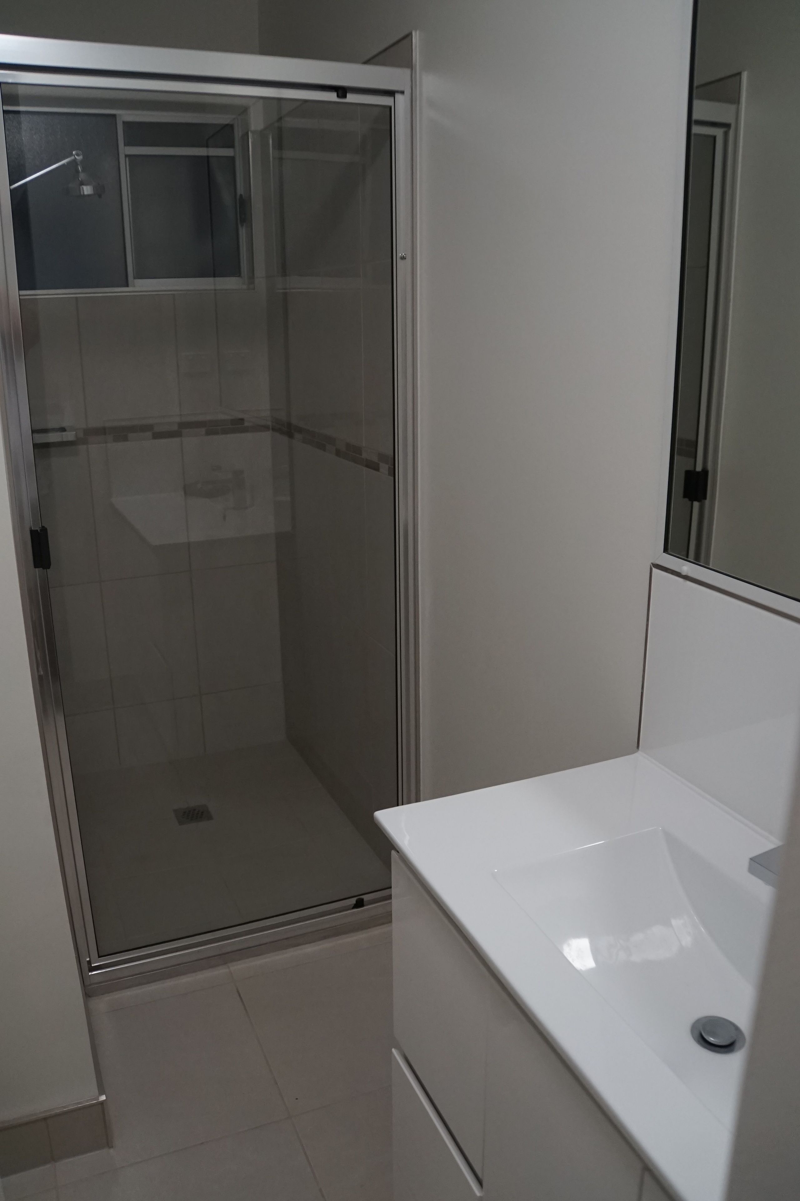 A small, modern bathroom with a glass shower enclosure, a white sink, and a mirror.