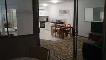 A modern kitchen with white cabinets, a dining area with a wooden table and chairs, and a TV in the living area.