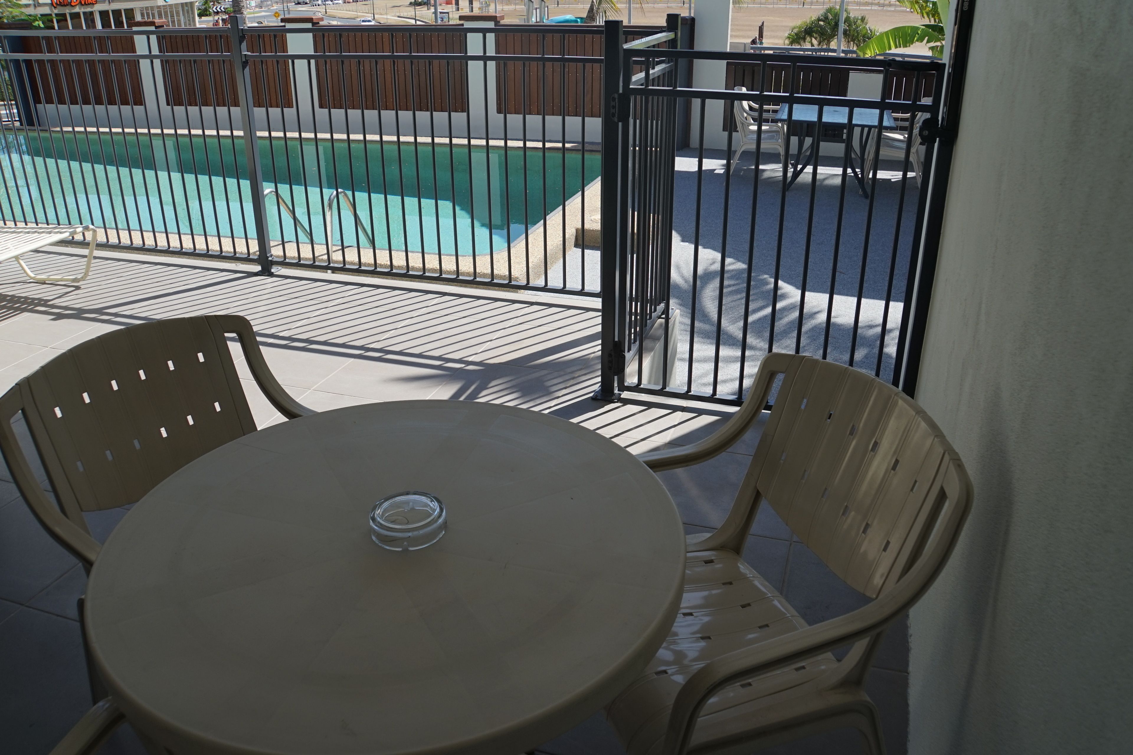 A balcony with a round table and two chairs, overlooking a swimming pool.