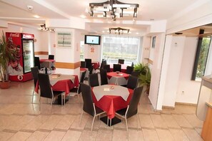 A dining area with tables and chairs, a Coca-Cola refrigerator, a television, and a window with a view. - Plus Hotel (Malu Mare)