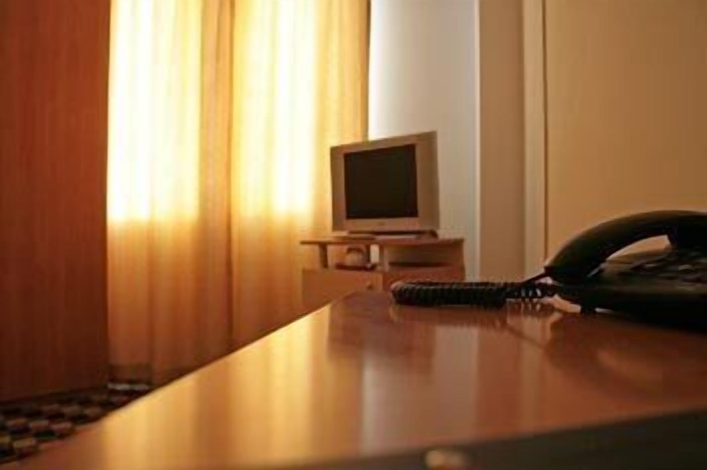 A hotel room with a wooden desk, a telephone, and a television on a small table.