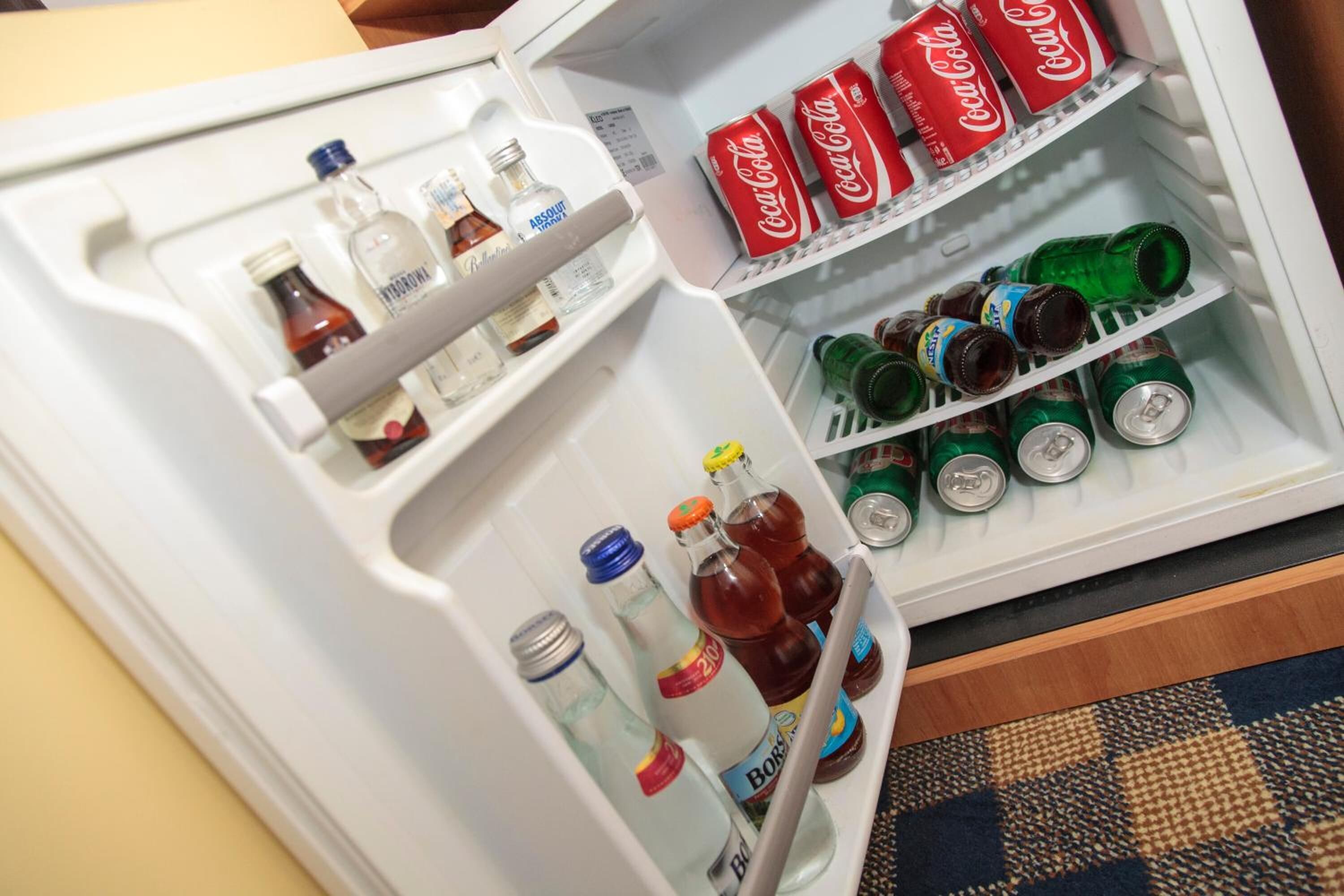 Un refrigerador con diversas bebidas, incluyendo latas de Coca-Cola, latas verdes y botellas.