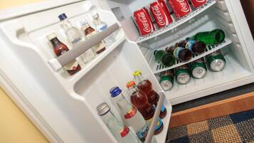 Un refrigerador con diversas bebidas, incluyendo latas de Coca-Cola, latas verdes y botellas.