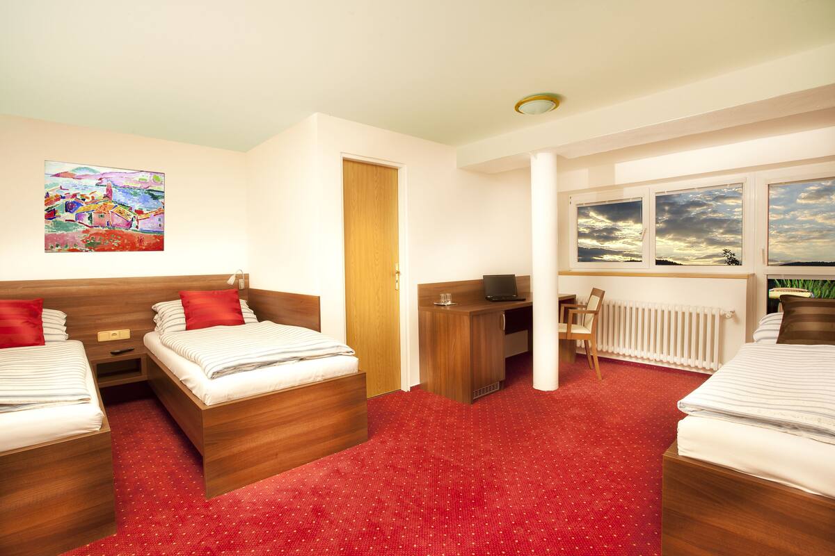 Et hotelværelse med to senge, et skrivebord, en stol, en radiator og et billede på væggen.