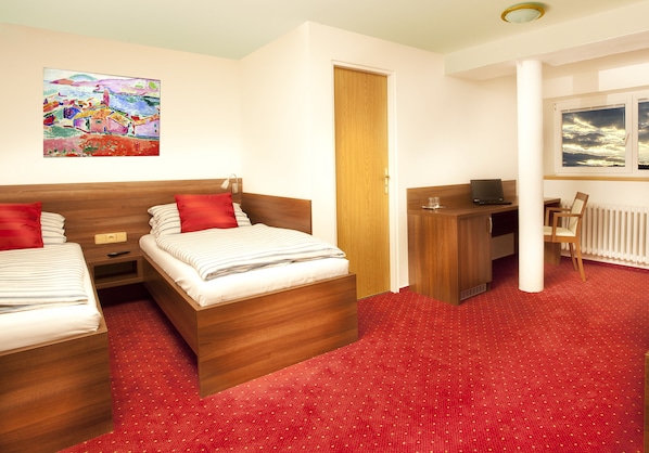 A hotel room with two wooden beds, a desk, a chair, a radiator, and a painting on the wall. - Pension Primus (Beroun)