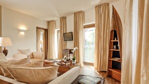 A hotel room with a sofa, armchairs, a wooden coffee table, a TV, and a bookshelf by a window with curtains. - ABION Villa Berlin (Berlin)