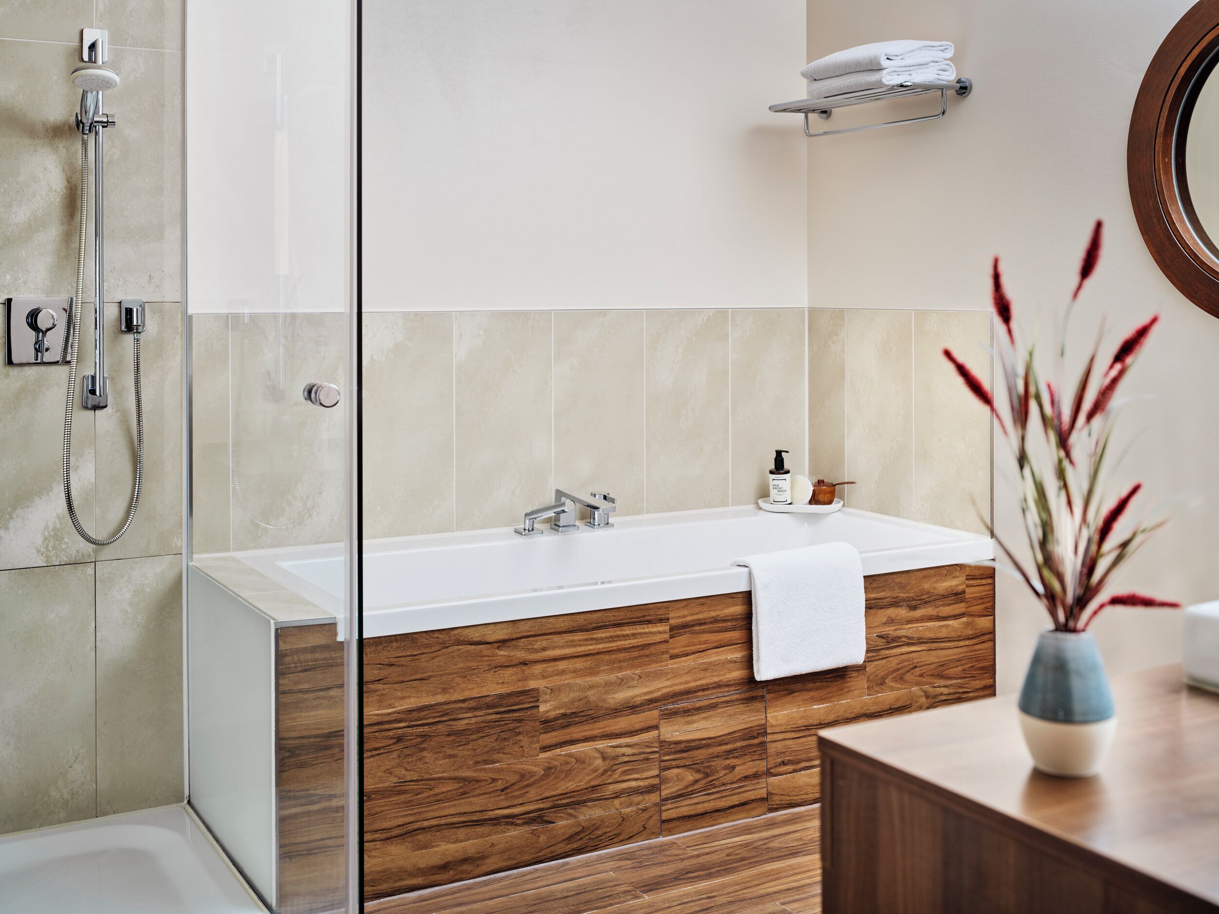 Un baño moderno con ducha envuelta en vidrio, tocador de madera, bañera blanca y un pequeño estante con toallas.