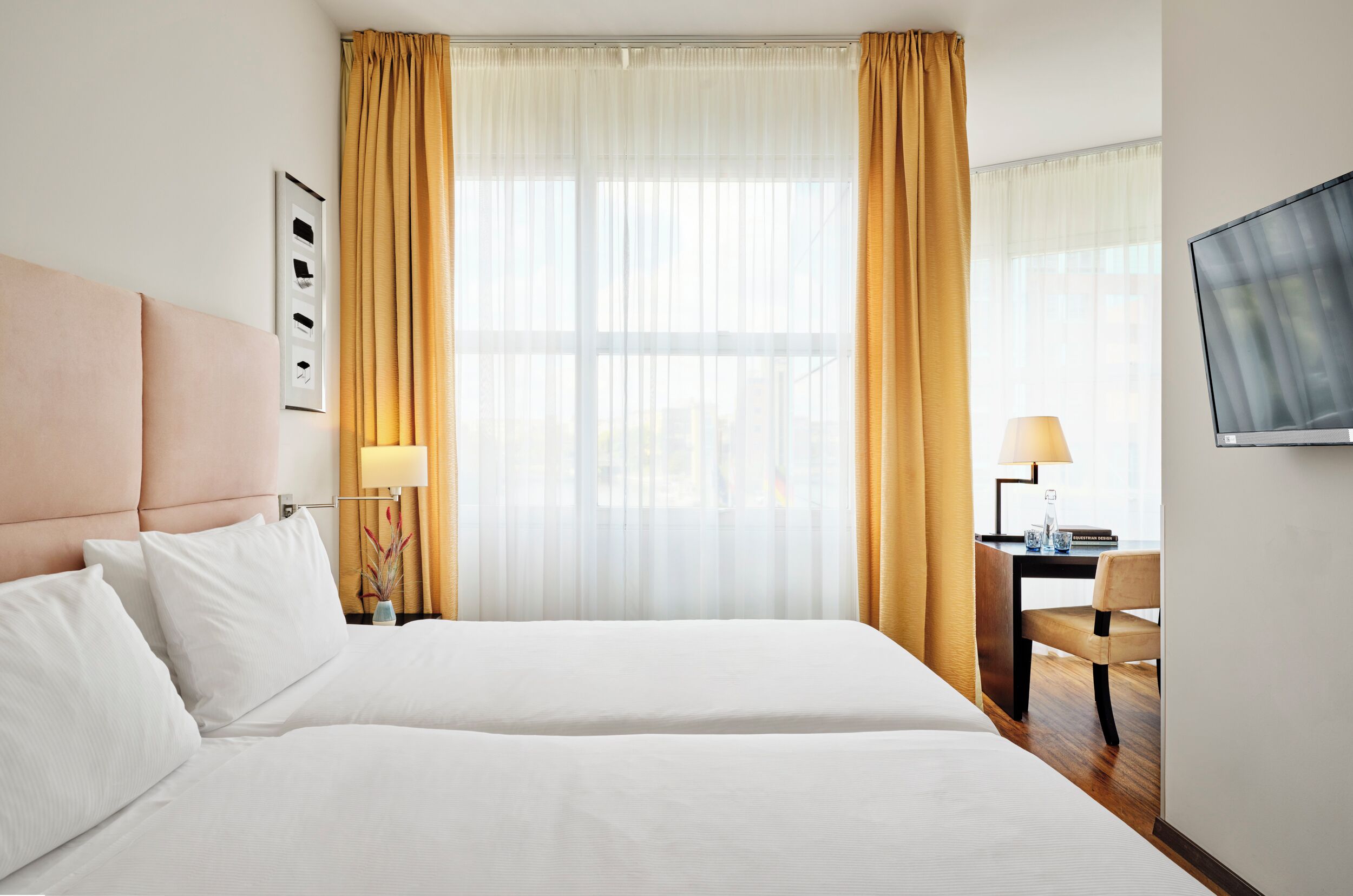 Ein Hotelzimmer mit einem großen Bett, einem Schreibtisch mit Lampe und einem Fernseher an der Wand.