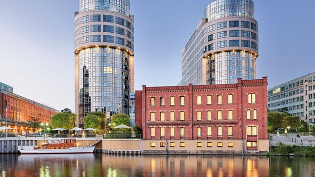 A waterfront view with two modern glass buildings, a historic brick building, and a boat docked in the foreground. - ABION Villa Berlin (Berlin)