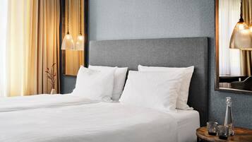 A hotel room with a large bed, two bedside lamps, a round wooden table with a bottle and glasses, and a mirror on the wall.