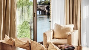 A room with a view of a river and a bridge, a beige sofa, and a wooden table with books. - ABION Villa Berlin (Berlin)