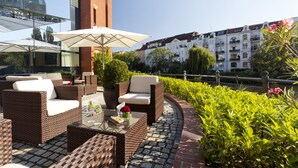 An outdoor seating area with wicker furniture and a glass table, overlooking a river and historic buildings. - ABION Villa Berlin (Berlin)