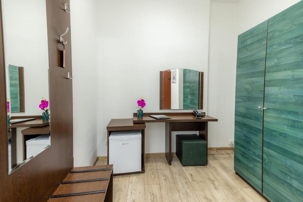 A compact room with a desk, a small refrigerator, a mirror, a wardrobe, and a bench.
