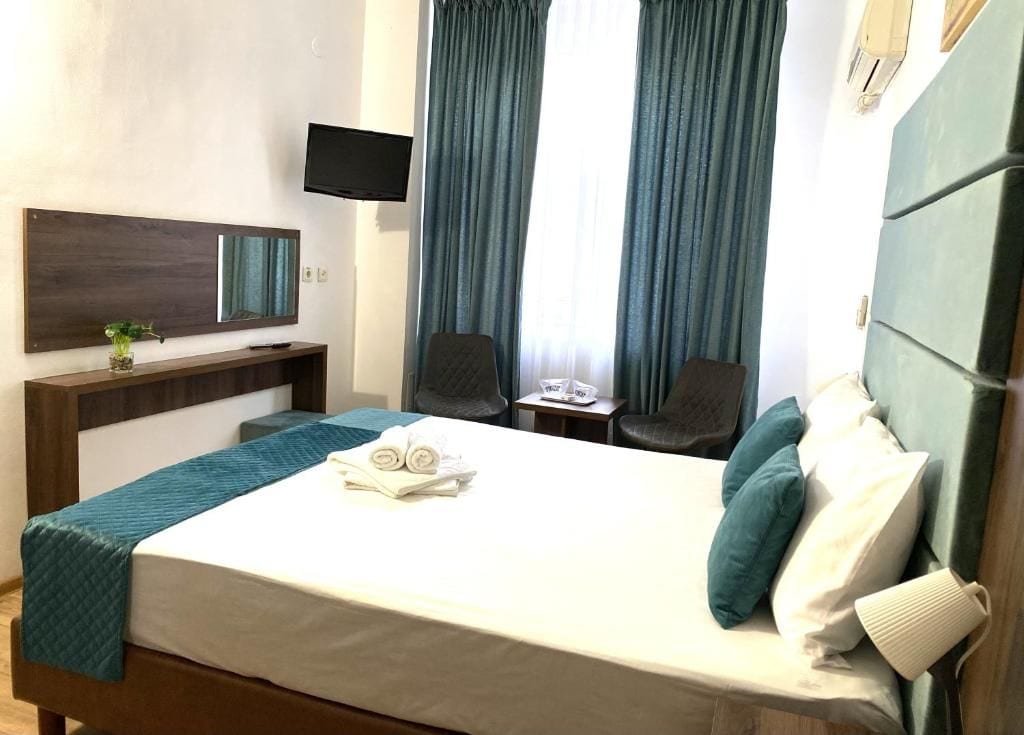 A hotel room with a bed, a desk, a chair, a TV, and a window with curtains.