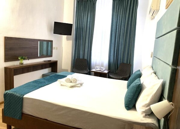 Une chambre d’hôtel avec un lit, un bureau, une chaise, une télévision et une fenêtre avec des rideaux.