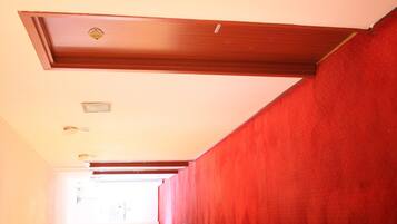 Un corridoio con tappeto rosso, travi in legno al soffitto e una porta visibile in fondo.