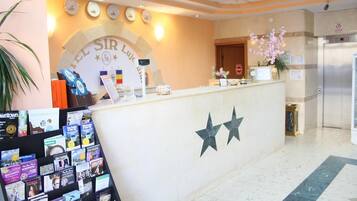 Una recepción de hotel con un reloj, un letrero que dice 'Hotel Sir Luis' y una exhibición de folletos.