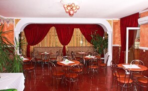 A restaurant with round tables and chairs, a red curtain backdrop, and a chandelier. - Sir Lujerului (Bucharest)