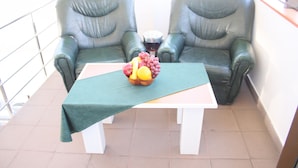 A balcony with two leather chairs, a table with a green tablecloth, and a bowl of fruit.