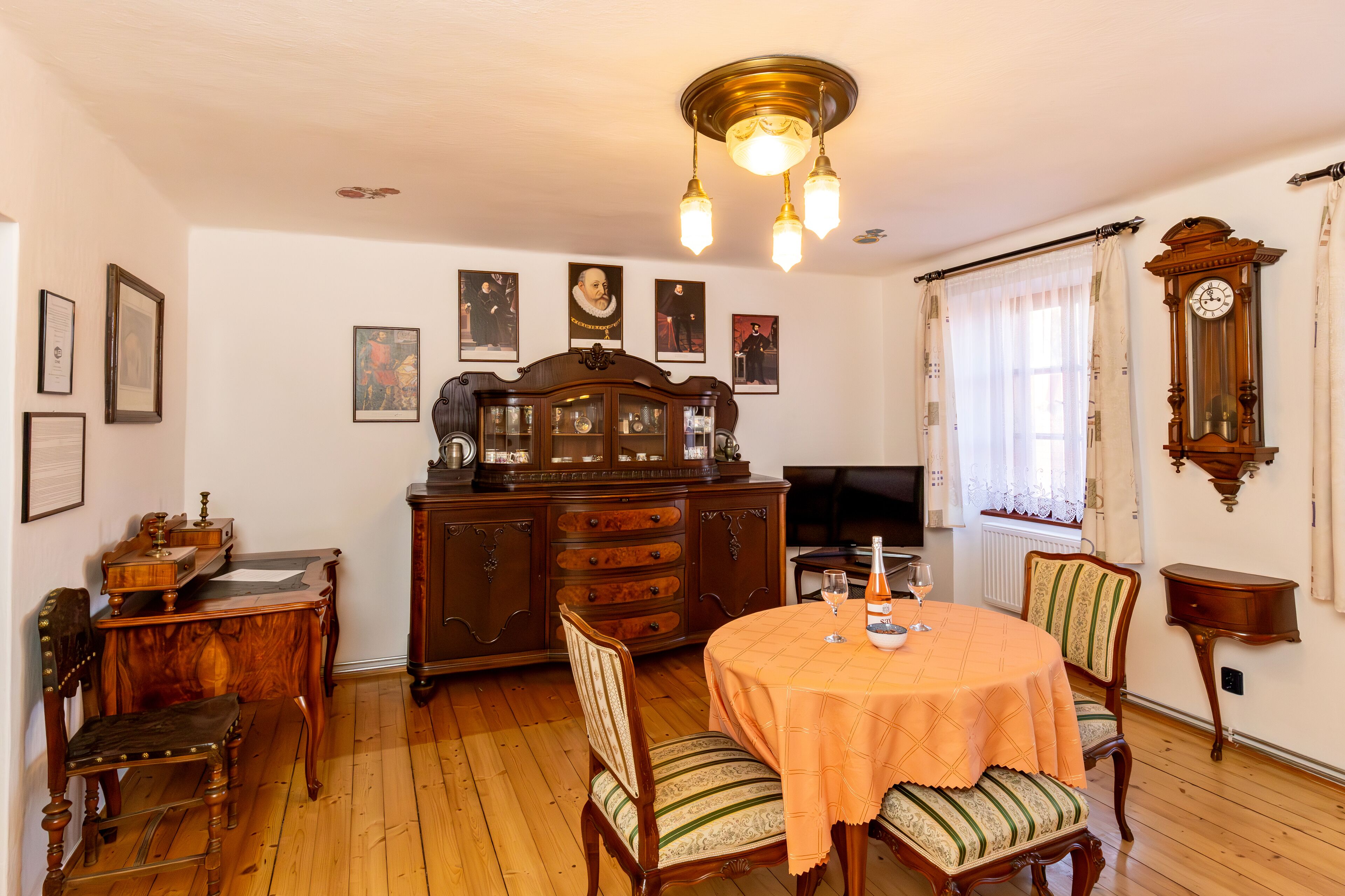 A dining room with a round table, chairs, a wooden cabinet, and a television.