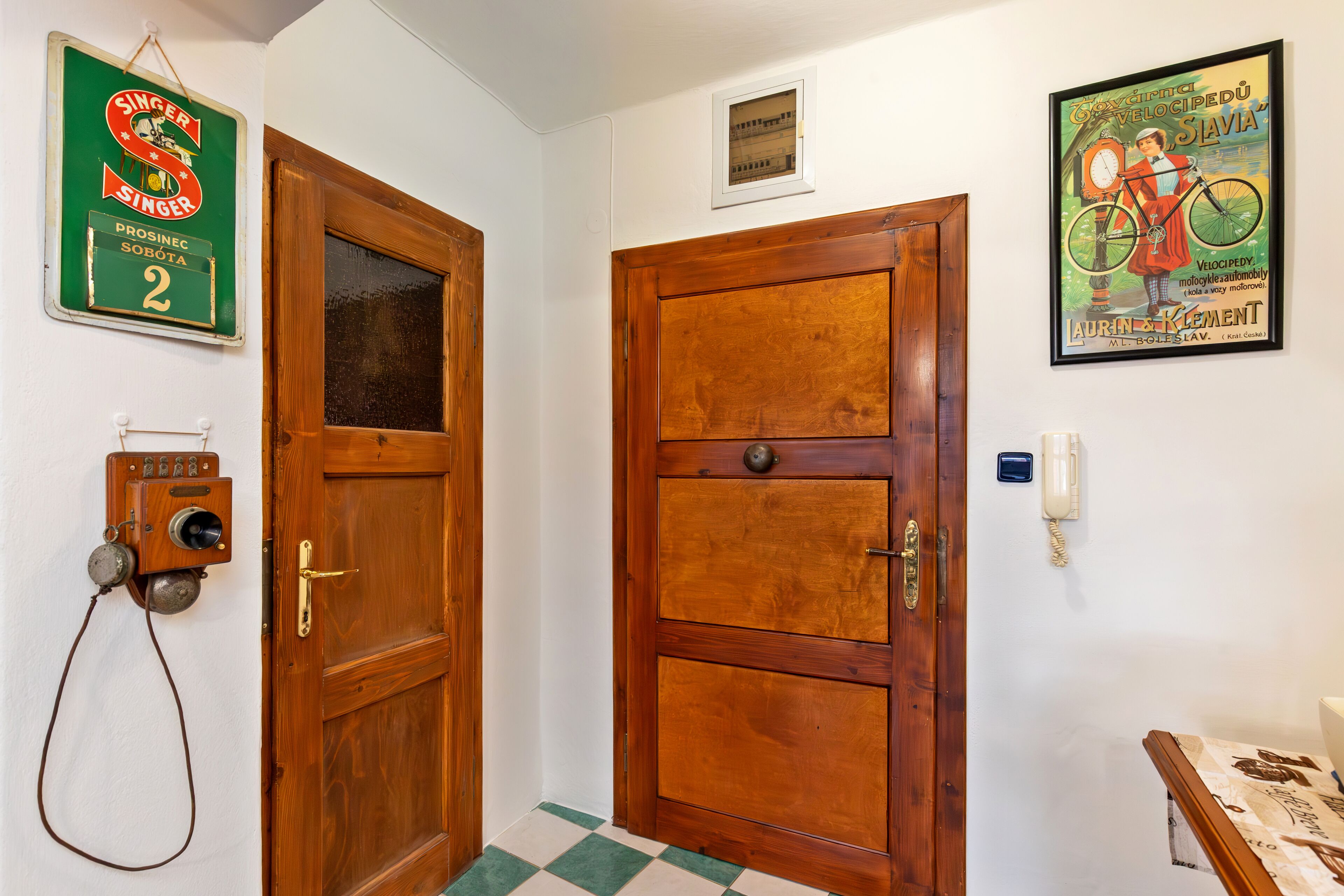 Un pasillo con puertas de madera, un teléfono antiguo y un cartel enmarcado en la pared.