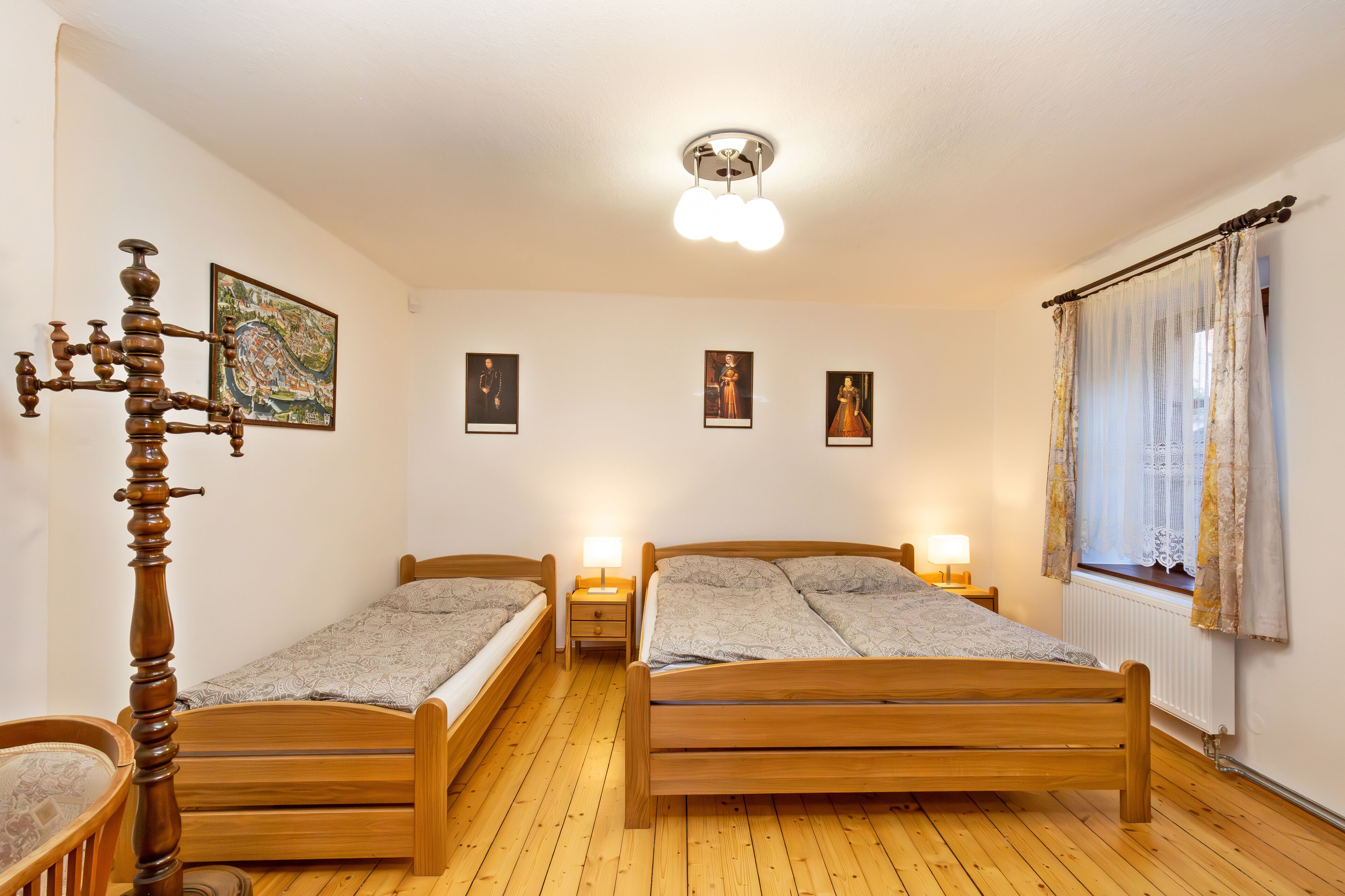 Un dormitorio con dos camas de madera, una silla de madera, una mesita de noche con lámpara y un candelabro en el techo.