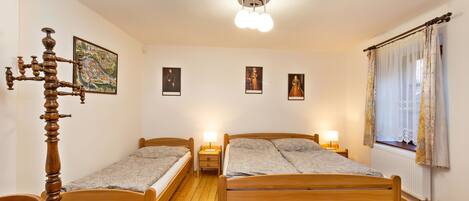 Un dormitorio con dos camas de madera, una silla de madera, una mesita de noche con lámpara y un candelabro en el techo.